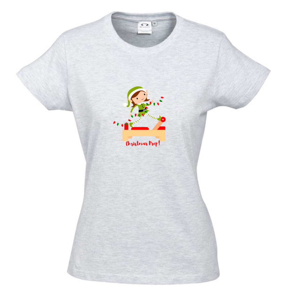 round neck, snow merle womens tee tee with an elf performing front splits pilates exercise on the reformer carrying christmas lights - with the title christmas prep