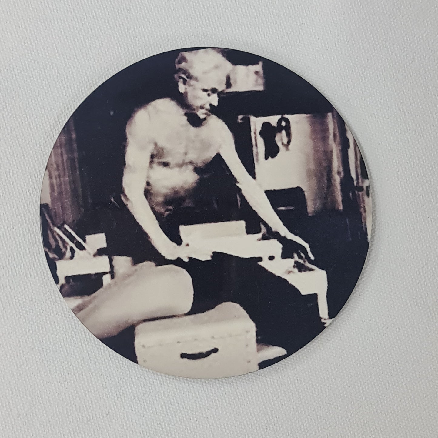 Round cork coaster featuring black and white photo of joseph pilates teaching climb a tree exercise on the reformer machine