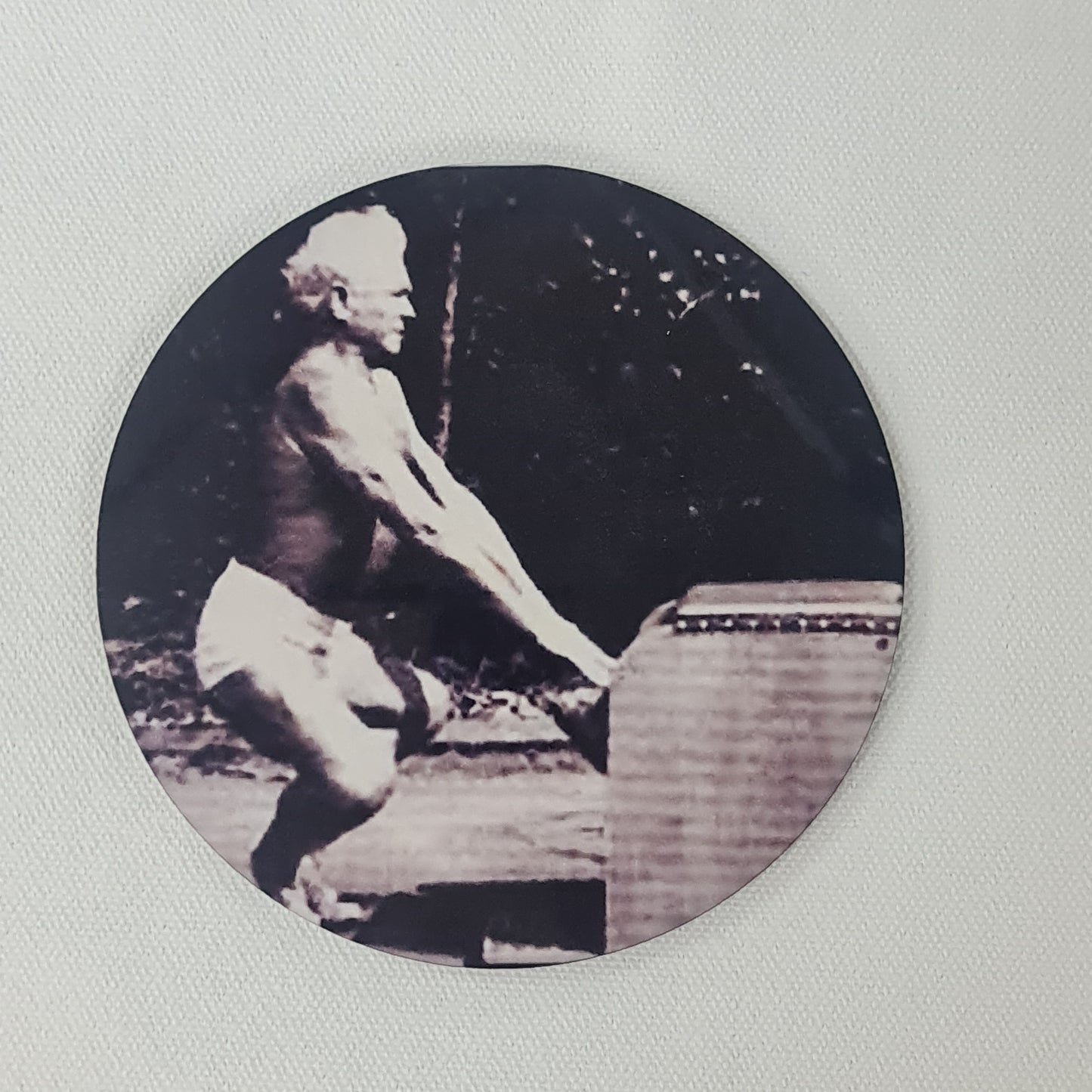 Round cork coaster featuring joseph pilates perfomring a forg squat on the wunda chair using arms press
