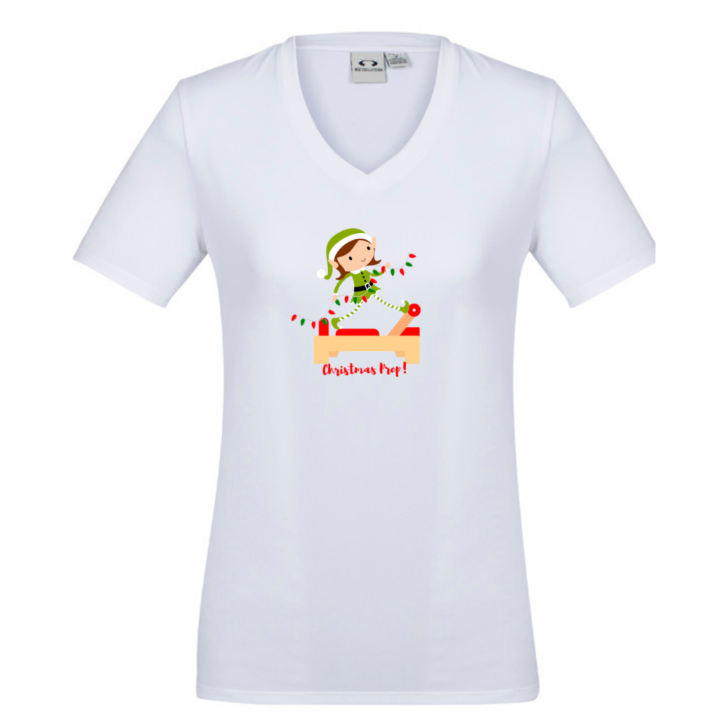 white v neck womens  tee with an elf performing front splits pilates exercise on the reformer carrying christmas lights - with the title christmas prep